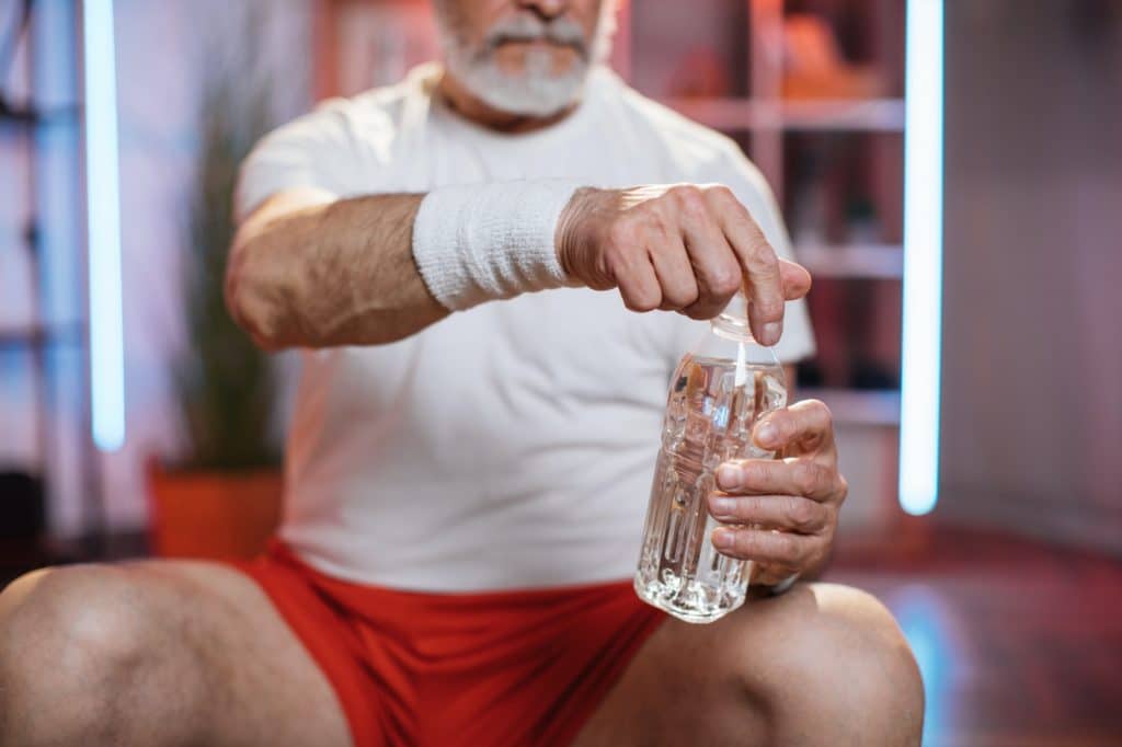Old man holding bottle of water while resting during workout
